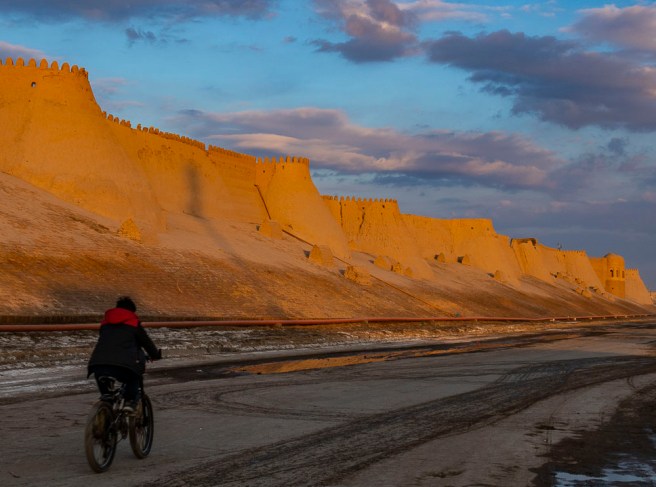 Boy biking along the city wall in Khiva